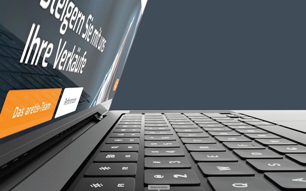 Laptop-Seitenansicht mit deutscher Website "Steigern Sie mit uns Ihre Verkäufe", orangefarbene Schaltfläche, grauer Hintergrund.