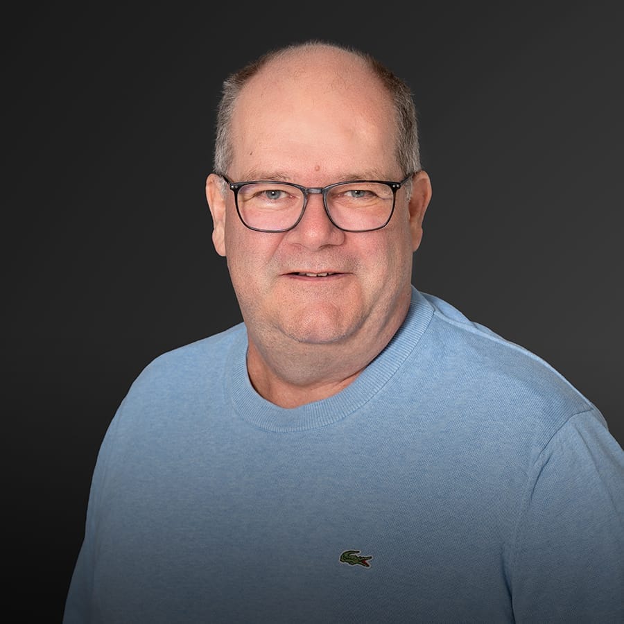 Mann mittleren Alters mit Brille, kurze graue Haare, hellblauer Pullover, leichtes Lächeln.